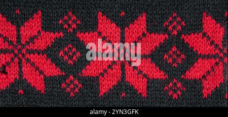 Red color eight pointed star knitted pattern on sweater. Red stars on black background, studio shot, indoors. Stock Photo