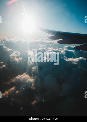 Airplane Wing Illuminated by Radiant Sunlight Above Puffy Clouds - Bright Aerial View at High Altitude Stock Photo