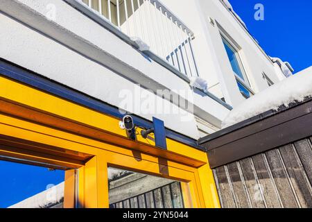 Solar-powered security camera mounted on yellow wall villa with solar panel, surrounded by snow in winter day. Stock Photo
