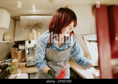 Asian female chef with ketchup squeeze bottle in hand taking order with light smile on face Stock Photo