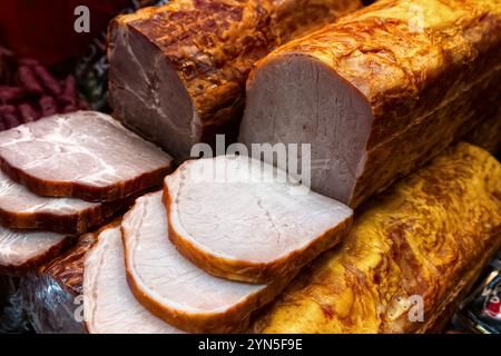 Various smoked pork hams in glass display case of butcher shop, top view. Stock Photo