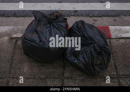 Two black plastic bags of trash are on the sidewalk. The bags are on the ground and are not being used. Stock Photo