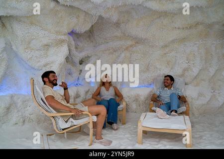 Three people are sitting in chairs in a cave-like room. The room is decorated with white furniture and has a blue light in the background. Scene is re Stock Photo