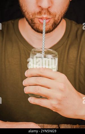 Close-up of a man drinking green matcha latte from a glass through a straw, tea culture concept. A man sips tea through a straw Stock Photo