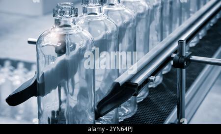 Glass bottles line on a conveyor belt. Bottles are transparent and clean. Stock Photo