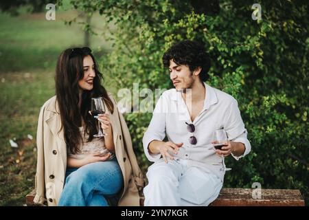A young couple enjoys a relaxed outdoor conversation, each holding a glass of red wine. Stock Photo