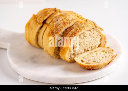 Rustic loaf of sourdough bread sliced thin on a marble cutting board Stock Photo