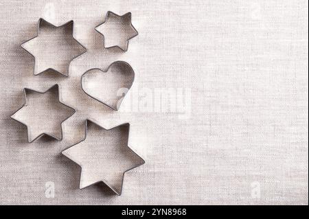 Cookie cutters on linen fabric, with empty space for text. Traditional biscuit cutters, tools to cut cookie and biscuit dough. Cutouts made of tin. Stock Photo