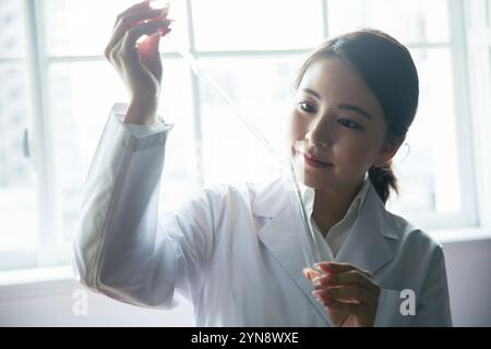 Researcher in her 20s using a dropper to fill a test tube with liquid Stock Photo