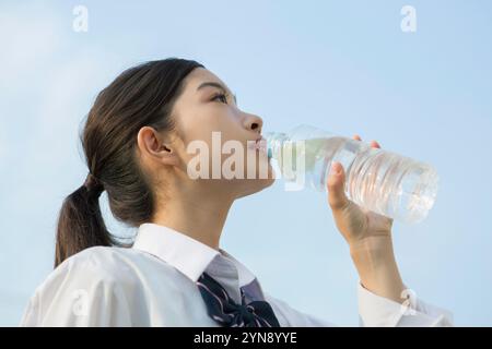 High school girl drinking water from a plastic bottle under a blue sky Stock Photo