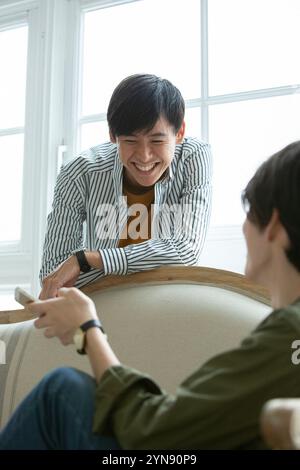 Two men in their 20s sitting on a sofa talking Stock Photo