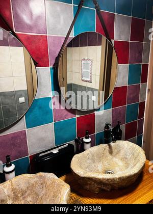 A contemporary bathroom featuring vibrant multicolored tiles, round mirrors, and unique stone sinks. The stylish design creates a modern and artistic Stock Photo