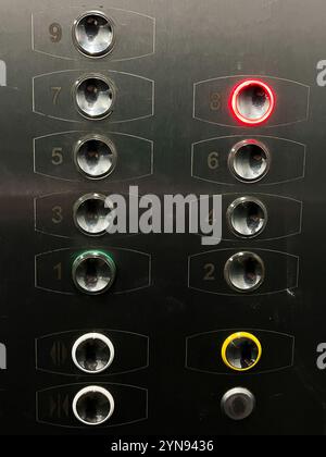 A detailed image of an elevator control panel with buttons highlighted in red and green, indicating active floors. Stainless steel surface with reflec Stock Photo