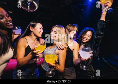 A group of friends celebrates on a fun night out at a vibrant nightclub, holding brightly colored cocktails and enjoying each other's company. Stock Photo