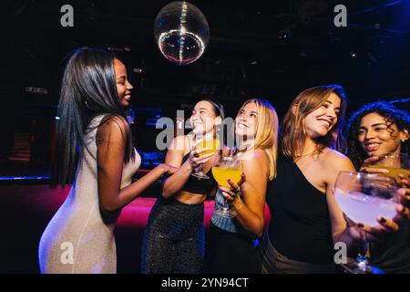 A lively group of friends enjoy a night out, dancing and celebrating under a disco ball in a vibrant nightclub setting. Stock Photo