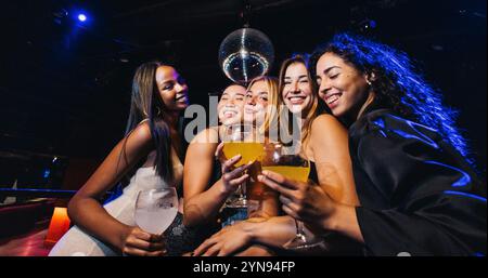 Group of friends enjoying drinks at a lively nightclub. Laughter and joy fill the scene as they celebrate together under the disco lights. Stock Photo