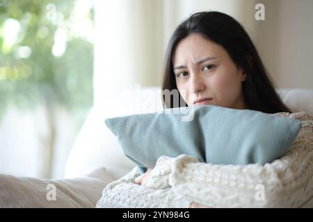 Sad asian woman looking at camera sitting on a couch at home Stock Photo