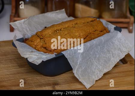 A freshly baked loaf of banana bread rests on a wooden cutting board, invitingly warm in a charming kitchen. Stock Photo