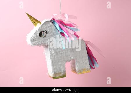 Bright pinata in shape of unicorn hanging on pink background Stock Photo