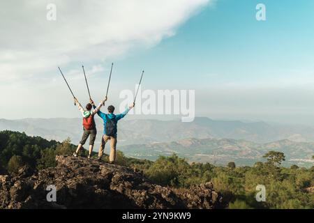 Adult couple celebrating success reaching mountain top together, arms raised in victory. Achievement and adventure lifestyle concept Stock Photo