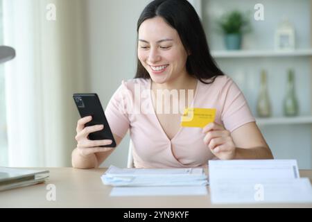 Happy asian woman paying invoices online using credit card and phone at home Stock Photo