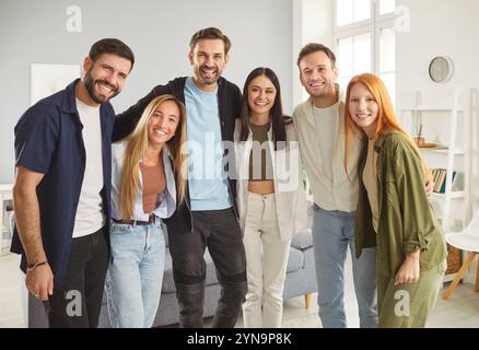Five happy young friends or colleagues standing in row, smiling and hugging while posing for photo. Stock Photo