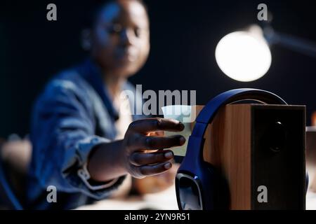 Picture of an African American female influencer with wireless headphones and a blue sticky note on a wooden stand. Close-up of a black woman placing a reminder note on the board. Stock Photo