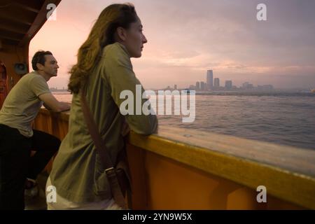 A man and a woman watch the sun setting over Manhattan from aboard a ferry in New York City, New York. Stock Photo