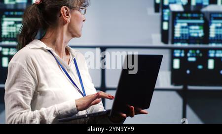 Trained IT consultant in server farm housing high end mainframes capable of quickly and efficiently performing complex computations and data analysis, using mockup laptop to clear risks Stock Photo