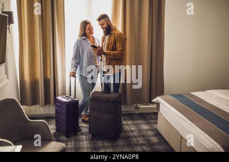 Young happy couple is on vacation. Tourists arrived in hotel room with their suitcases. Stock Photo