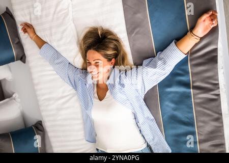 Young happy woman is on vacation. Tourist arrived in hotel room and relaxing on bed. Stock Photo