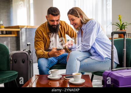 Young happy couple is going on vacation. Tourists sitting in hotel lobby and drinking coffee. Stock Photo