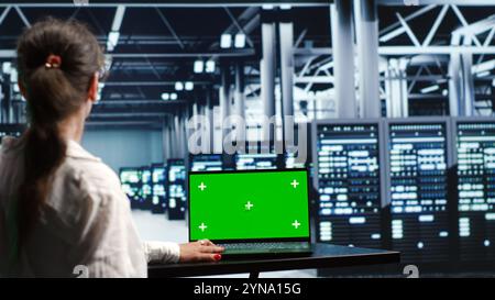 Certified IT programmer in server farm housing high end clusters capable of quickly and efficiently performing complex computations and data analysis, using mockup laptop to eliminate issues Stock Photo