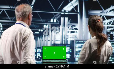 Licensed IT admins looking around high tech data center, using chroma key laptop to crosscheck disaster recovery plan and assess server systems in need of replacement, preventing collapse Stock Photo