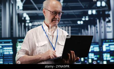 Qualified IT professional navigating network of servers in industrial location. System administrator with laptop ensuring seamless operations, doing optimizations and maintenance in data center Stock Photo