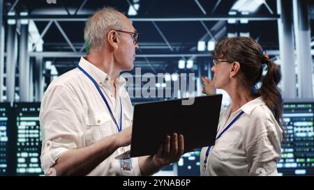 IT developers in data center using laptop to monitor energy efficient mainframes. Server rows using renewable sources employed to minimize consumption and reduce overall facility carbon footprint Stock Photo
