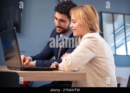 Business partners collaborating on laptop in modern office, smiling and working. Stock Photo