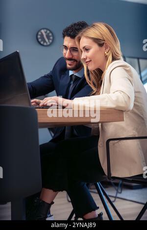 Business partners collaborating on laptop in modern office, smiling and working. Stock Photo