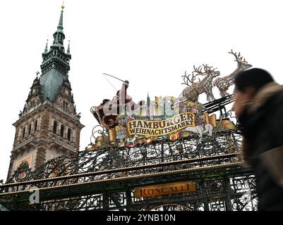 Hamburg, Germany. 25th Nov, 2024. A woman (r) walks past the entrance to Hamburg's Christmas market, while the town hall building can be seen in the background. The Christmas market at Hamburg's Rathausmarkt was officially opened on Monday. Credit: Niklas Graeber/dpa/Alamy Live News Stock Photo