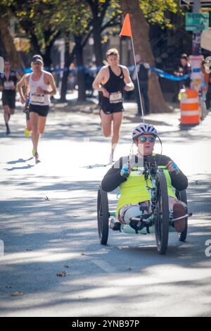 A handicapped athlete with only 1 leg operates a hand powered 3 wheel tricycle during the 2024 New York Marathon around the 10 mile mark in Brooklyn. Stock Photo