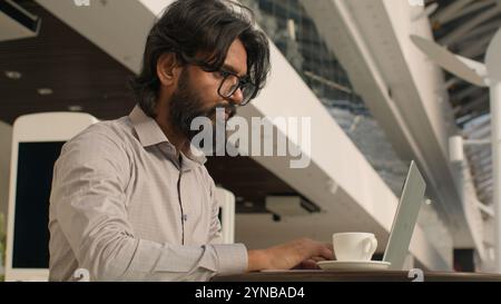 Pensive Indian businessman typing on laptop remote working internet concentrated arabian man manager analyzing digital data create business plan using Stock Photo
