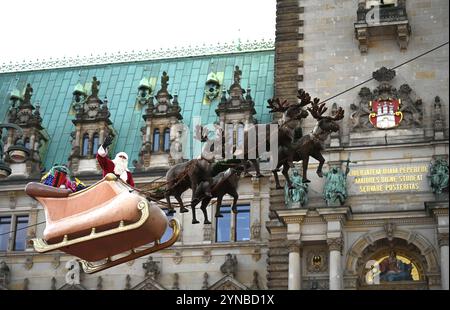 Hamburg, Germany. 25th Nov, 2024. A person in a Santa Claus costume waves to the crowd in front of the town hall on a sleigh with reindeer hanging from a rope over the Christmas market. The Christmas market at Hamburg's Rathausmarkt was officially opened on Monday. Credit: Niklas Graeber/dpa/Alamy Live News Stock Photo