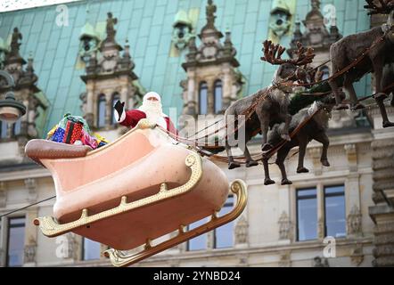 Hamburg, Germany. 25th Nov, 2024. A person in a Santa Claus costume waves to the crowd in front of the town hall on a sleigh with reindeer hanging from a rope over the Christmas market. The Christmas market at Hamburg's Rathausmarkt was officially opened on Monday. Credit: Niklas Graeber/dpa/Alamy Live News Stock Photo