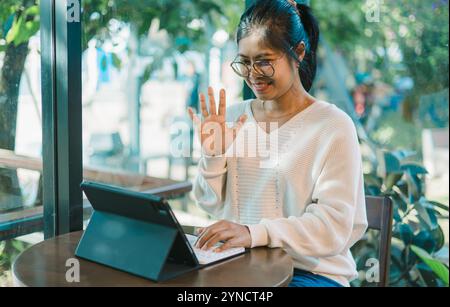 Asian woman is smiling as she has a video call with her friends or family, Sitting at desk, Using laptop computer, Having video chat, education concep Stock Photo