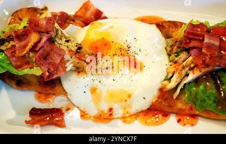 Top view flat lay of English breakfast style tapas with fried eggs, bacon, chicken, salad and chili salsa on toasted flatbread rustic gourmet food Stock Photo