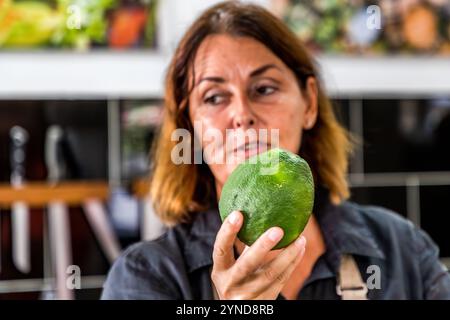 Helmi Smeulders is holding a Lahara orange (Citrus × aurantium, also known as Laraha) at her cookery school on Djonora Marthaweg, Willemstad, Curaçao. This variety of bitter orange, native to the island, provides the dried peel that gives Senior & Co.’s Original Curaçao Liqueur its characteristic flavour. Kòrsou, Curacao Stock Photo