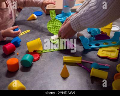 Mother and daughter bond over creative play with play-doh, creating colorful waffles and ice cream on table filled with molds and tools Stock Photo
