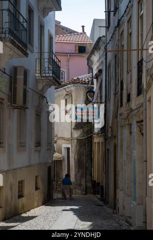 A person enjoying a coffe outside in a narrow street of Coimbra, Portugal. Tall buildings limit the tight on these streets, covered in shadows. Stock Photo