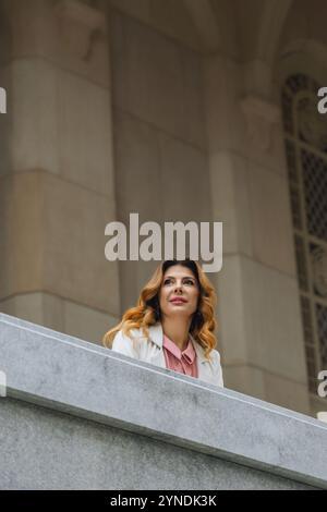 Woman Balcony Building - A woman stands on a balcony overlooking a building, looking up at something in the distance. Stock Photo