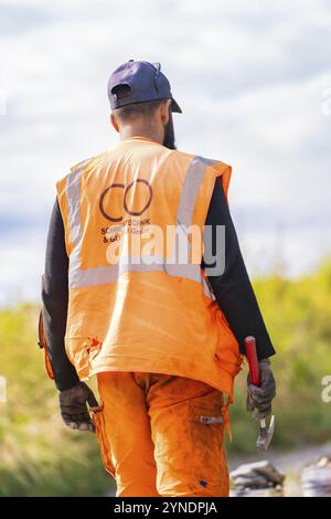 Worker in orange safety waistcoat holding hammer, standing outside with view into the distance, rail welding, track construction Hermann Hessebahn, Ca Stock Photo